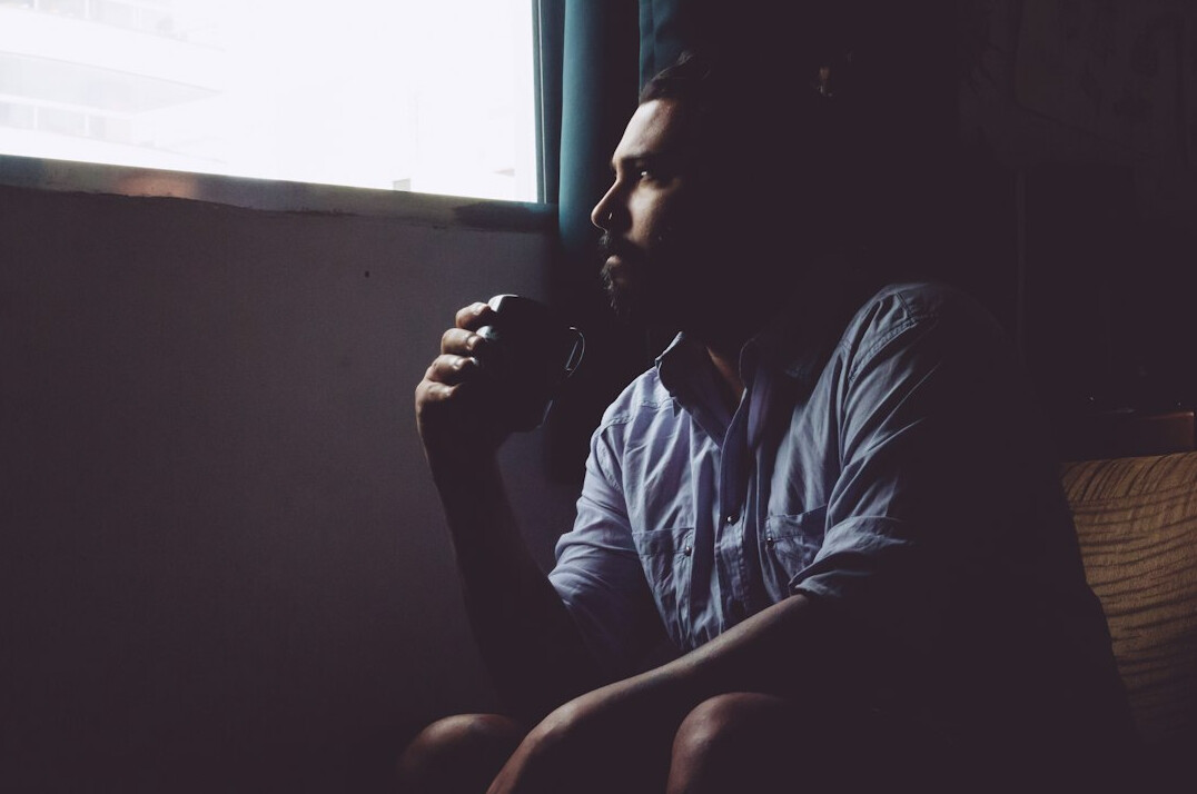 Young Brazilian man journaling by a window with a cup of tea